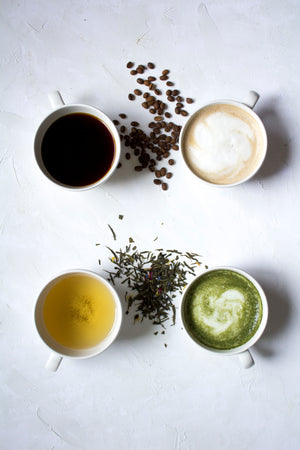 A photo of whole bean coffee and loose tea leaves with brewed coffee and tea in four mugs